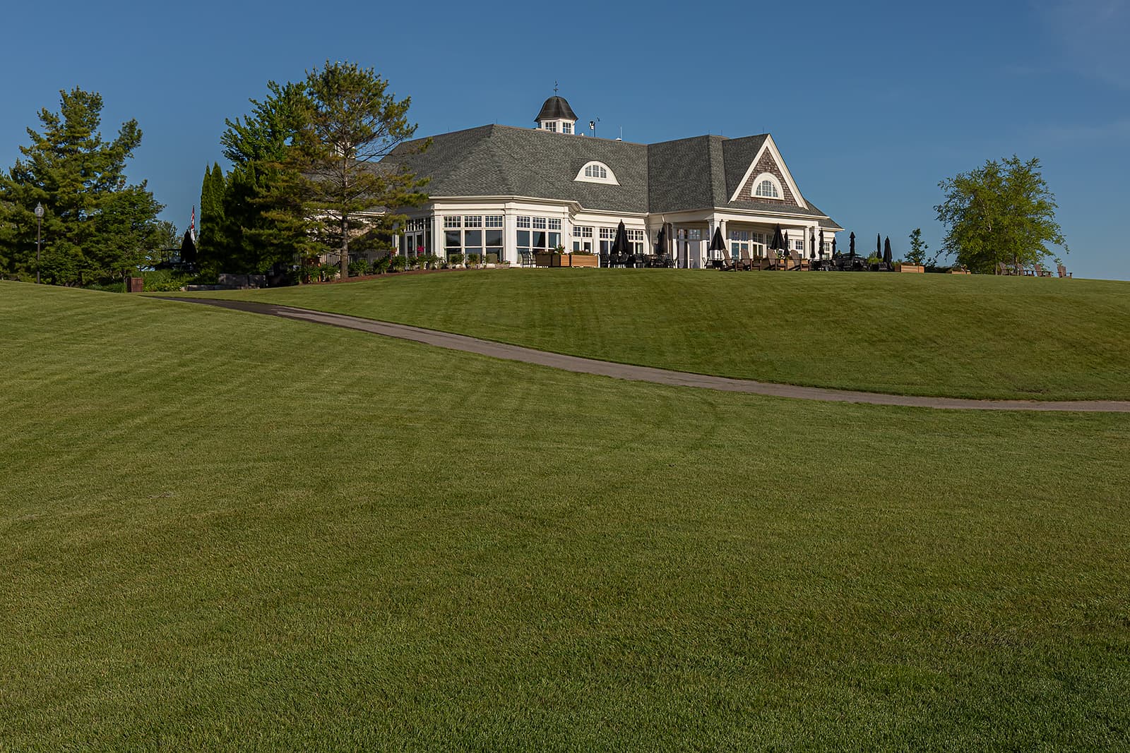elegant golf course clubhouse on hill with manicured lawn and cart path