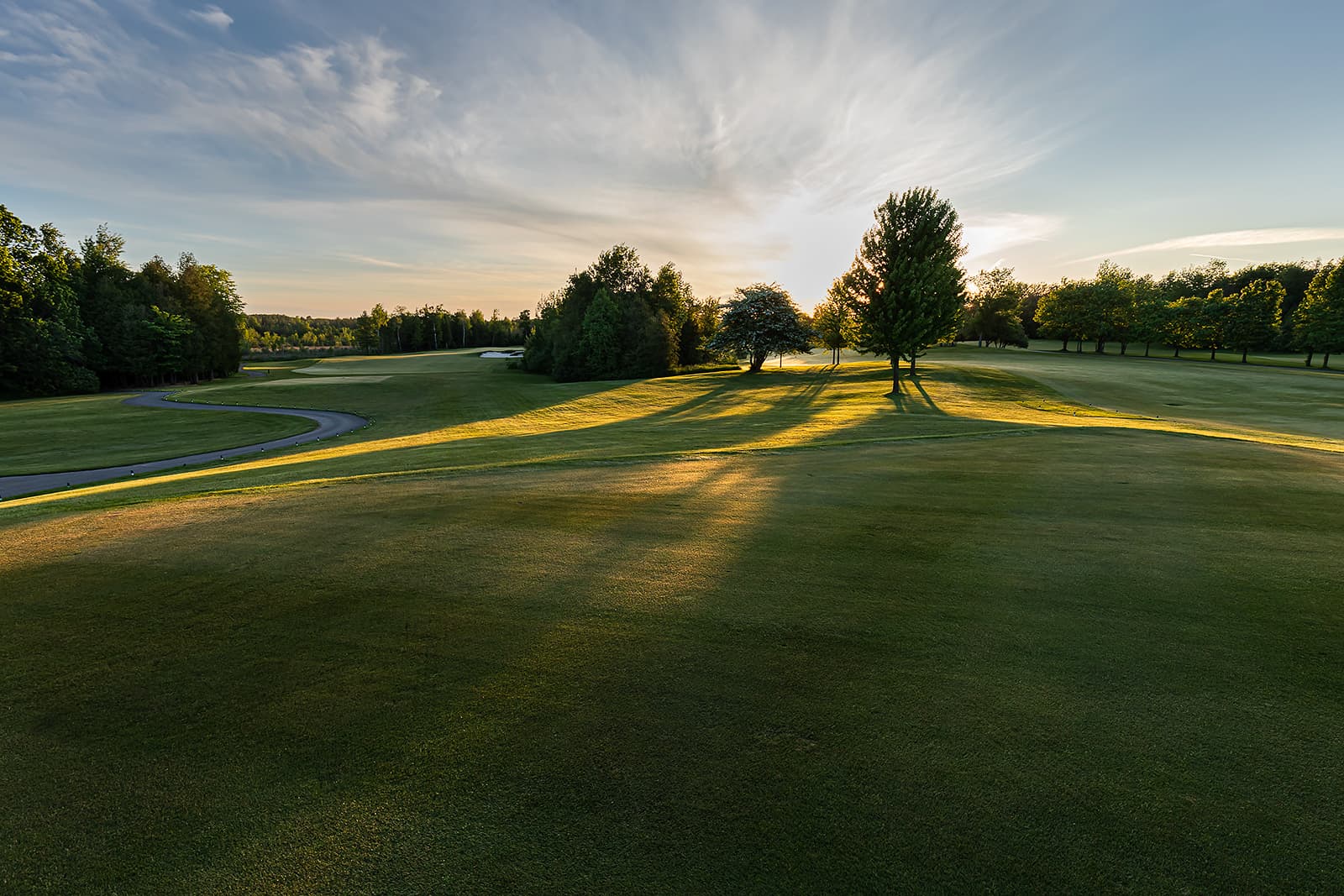 sunrise golf course fairway with trees and cart path