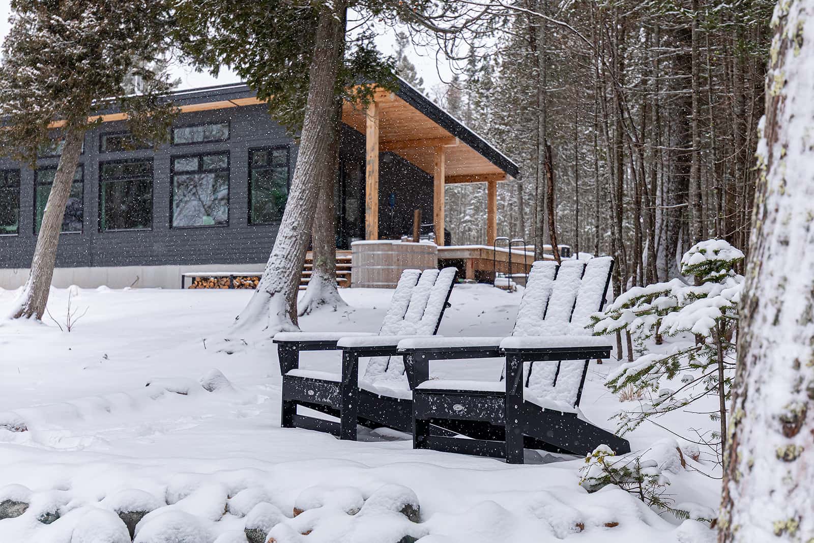 muskoka chairs in front of cabin during a snowfall