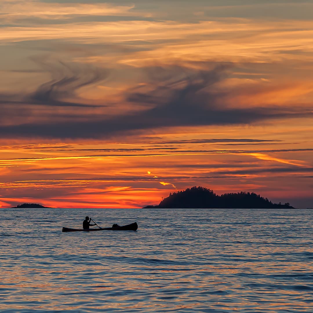 A silhouette of a man paddling a canoe at sunset