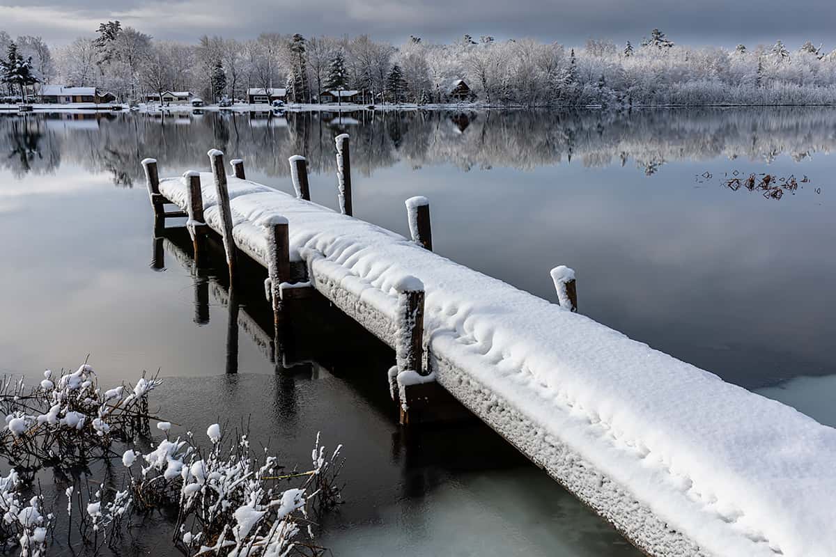 winter wonderland, river reflections and dock in a snow covered landscape