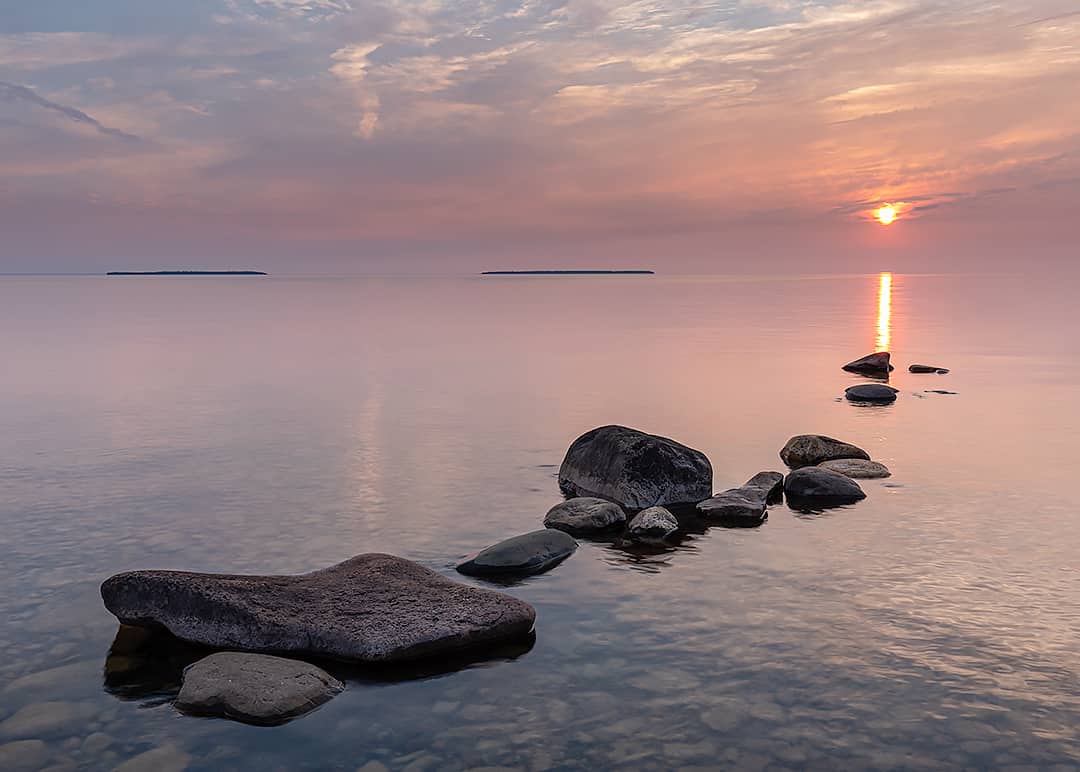 sunset on calm lake with rocks in foreground 